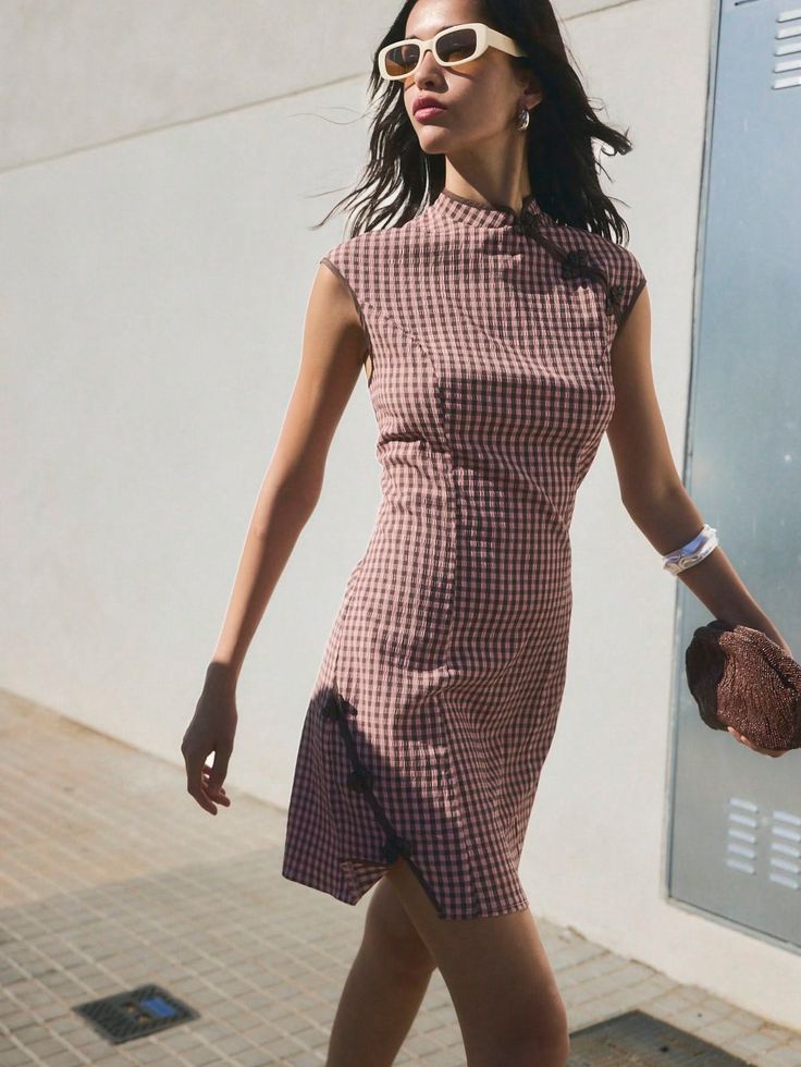 Woman in a gingham dress and sunglasses walking outdoors in daylight