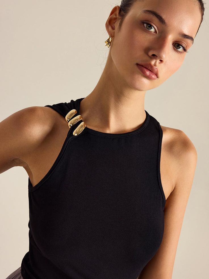 Woman in a black top with gold shoulder detail and earrings in a studio shot