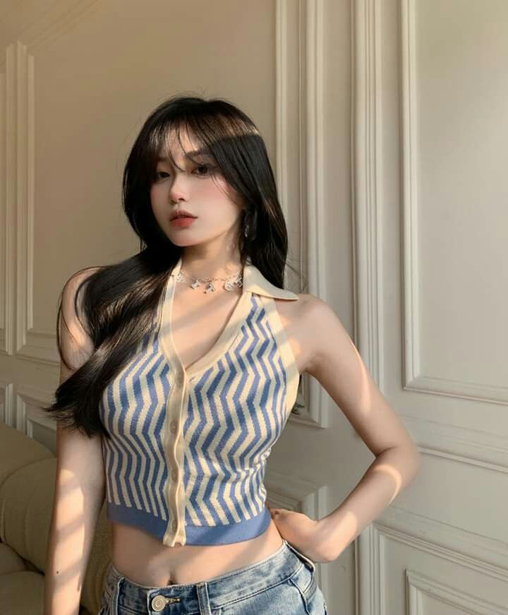 Woman with long black hair wearing a striped crop top and jeans indoors