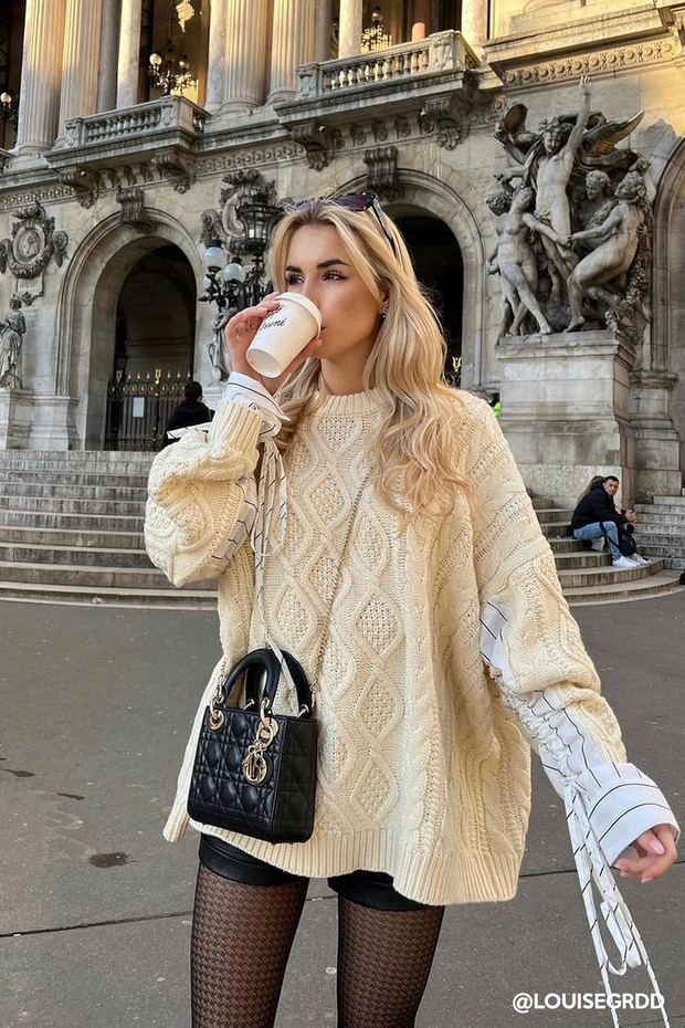 Blonde woman in a cable knit sweater and houndstooth tights drinking coffee outdoors