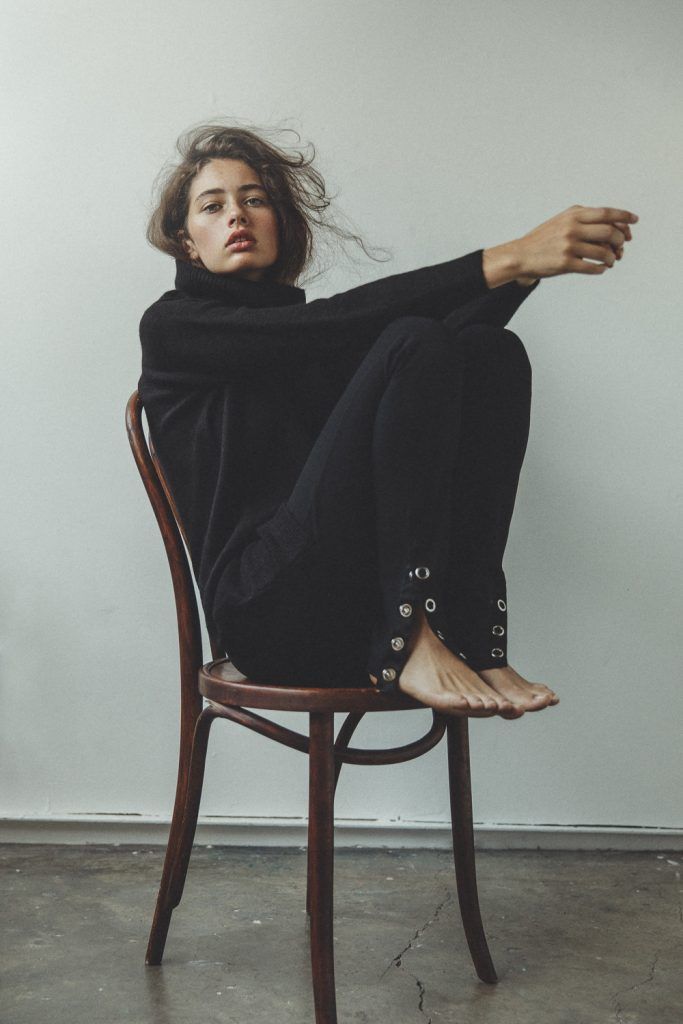Woman in a black turtleneck sweater and pants sitting on a wooden chair