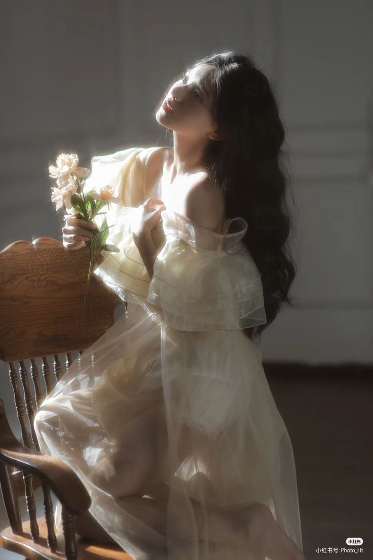 Woman in a sheer dress holding flowers, bathed in soft light