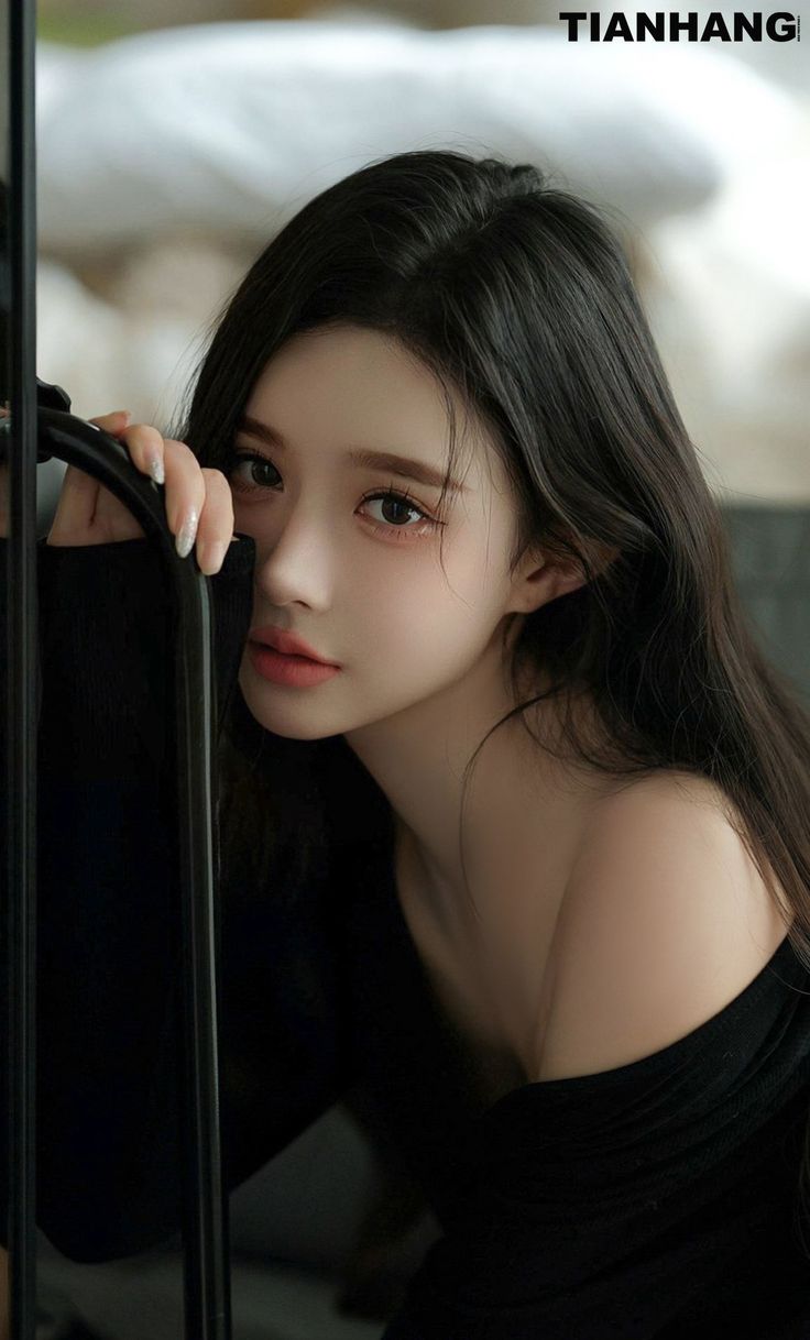 Woman with long black hair wearing an off-shoulder top, looking at the camera