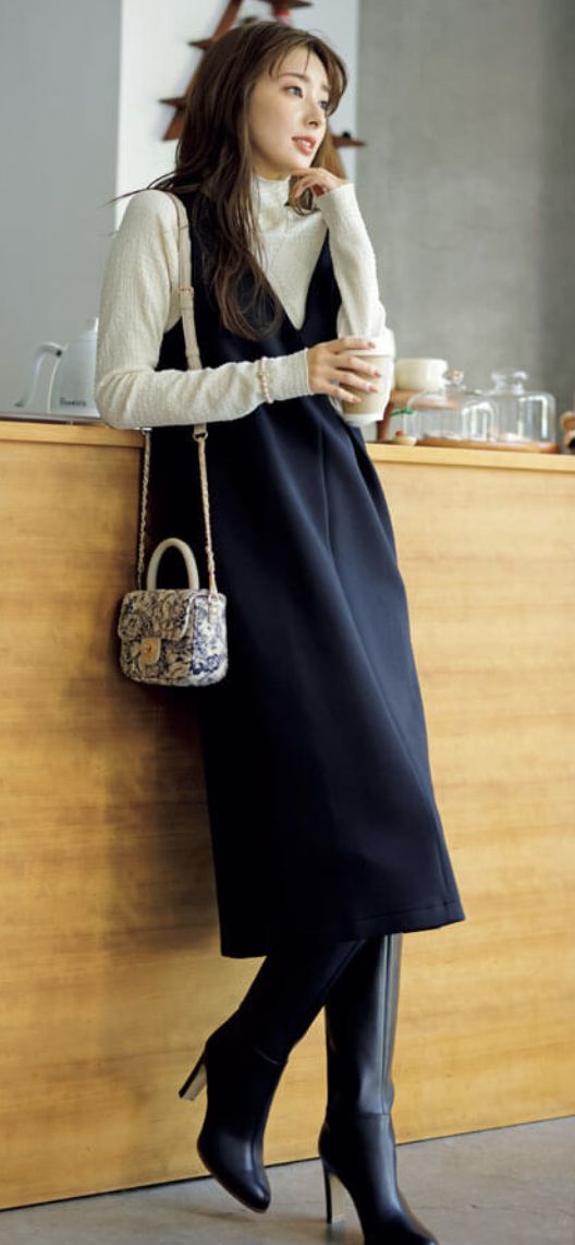 Woman in a black dress and white turtleneck holding a cup indoors