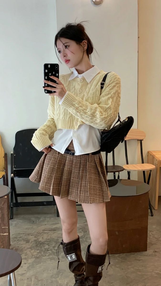 Woman in a plaid skirt and cropped cardigan taking a mirror selfie