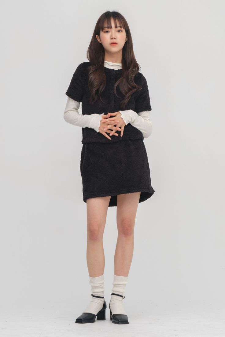 Woman in a black fuzzy top and skirt with white long sleeves and socks