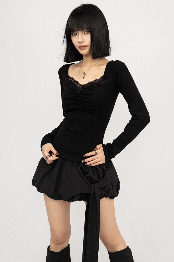 Woman with a black bob and bangs wearing a black top and mini skirt