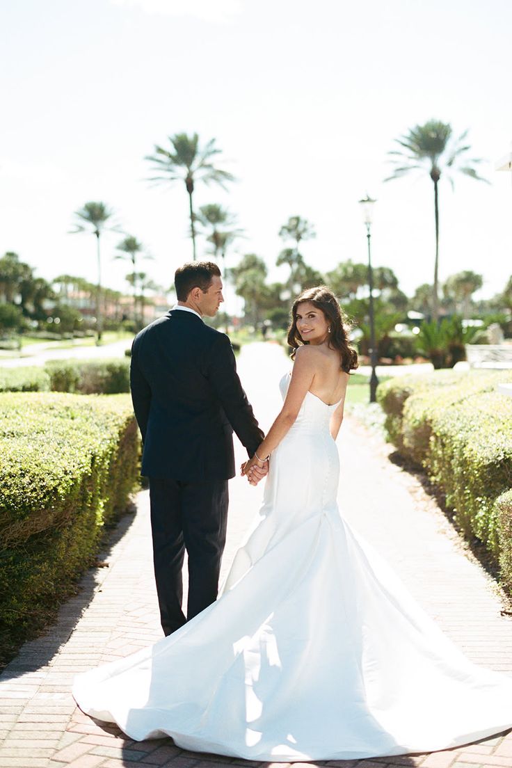Couple in wedding attire holding hands and walking outdoors with palm trees