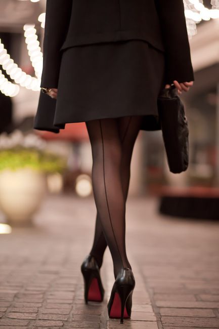 Woman in a black dress and seamed stockings walking away at night