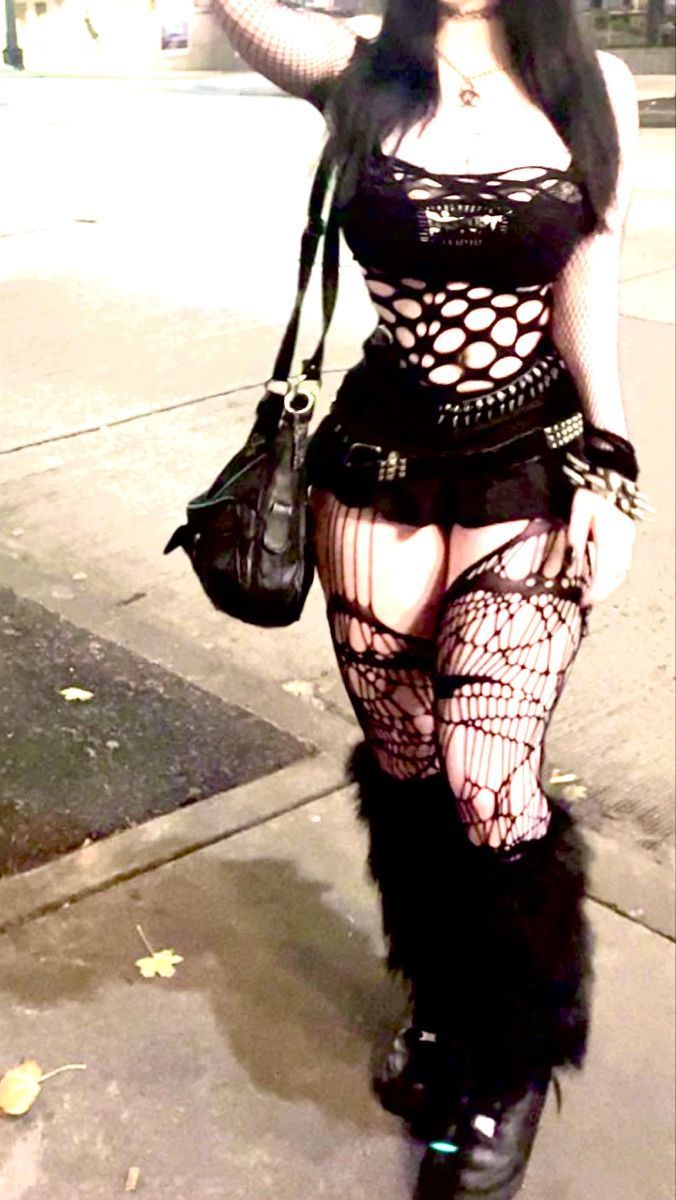 Woman in gothic attire with fishnet top and stockings outdoors at night