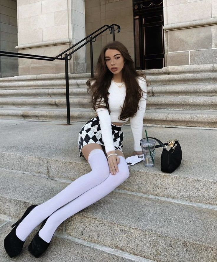 Woman with long hair wearing a crop top and mini skirt sitting on stone steps