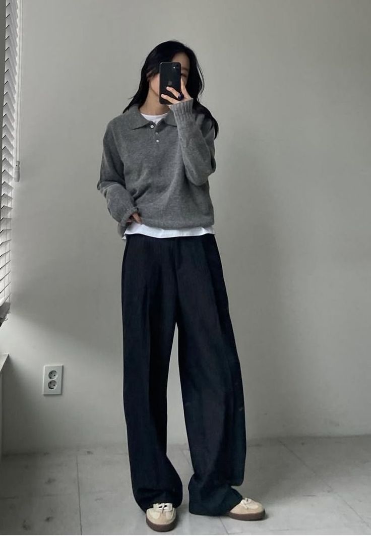 Woman in a gray sweater and wide leg pants taking a mirror selfie