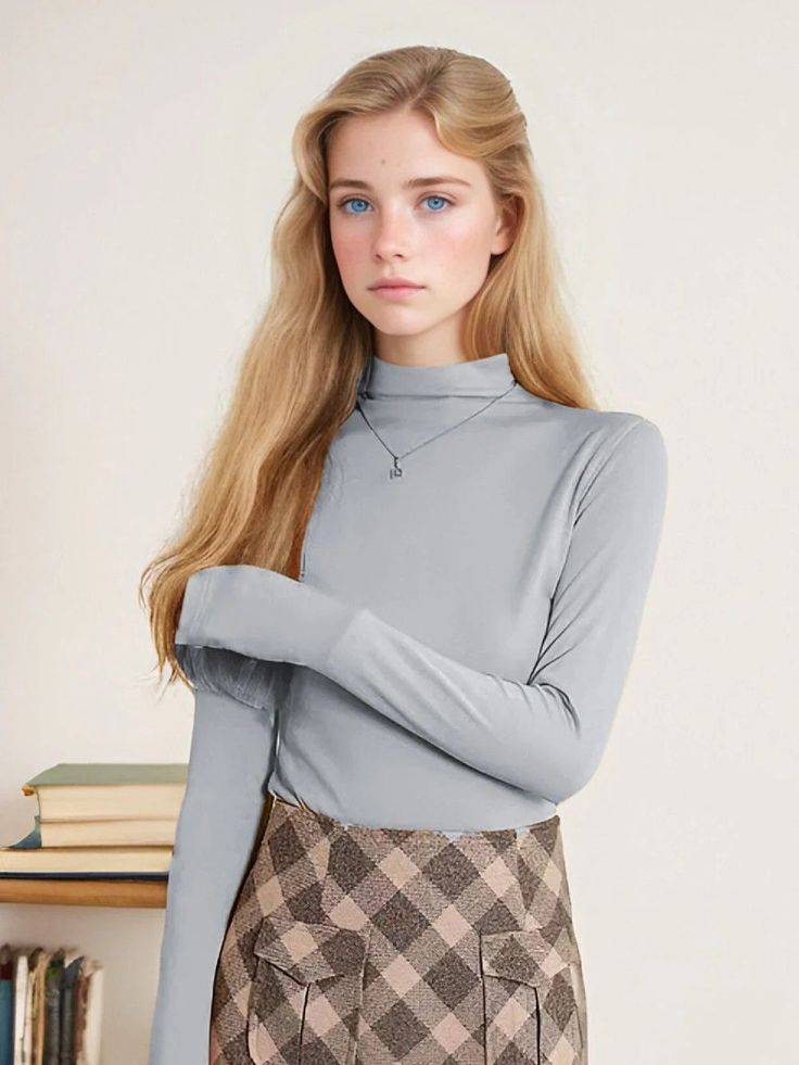 Young woman with blonde hair and blue eyes wearing a turtleneck and plaid skirt