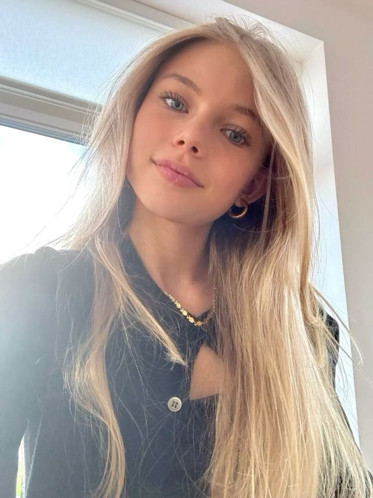 Young woman with long blonde hair and blue eyes wearing a black top and gold jewelry