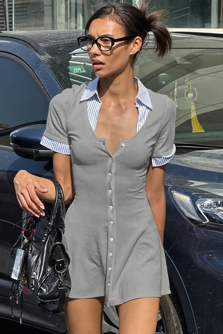 Woman in a gray dress and glasses standing outdoors