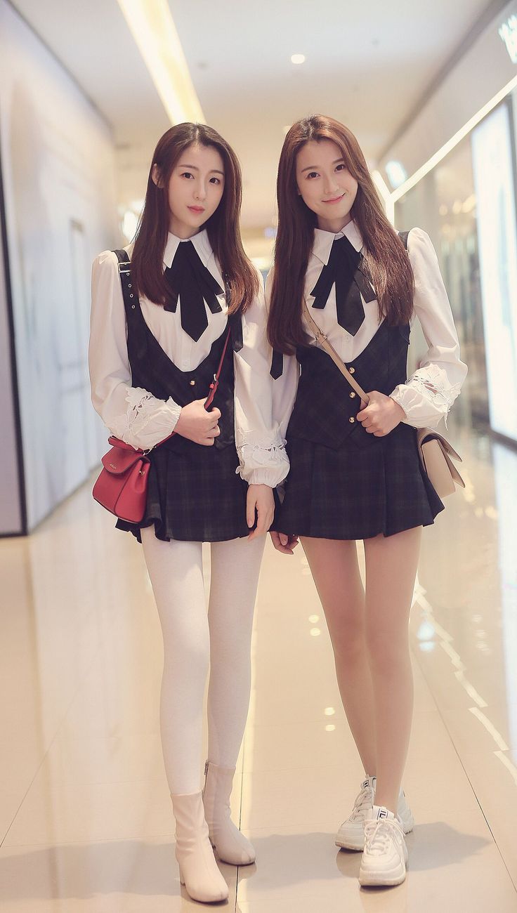 Two women in school uniform style outfits standing in an indoor setting