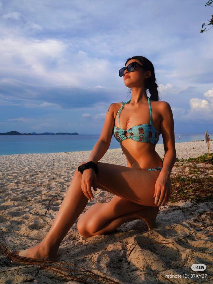 Woman in a bikini and sunglasses posing on a sandy beach at golden hour