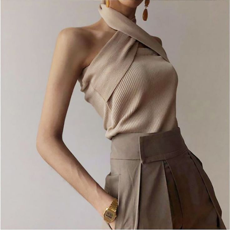 Woman in a beige halter top and pleated pants with a gold watch
