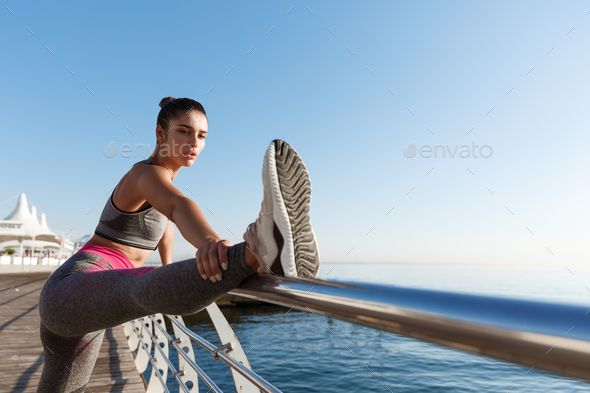 Woman in athletic wear stretching on a pier by the ocean