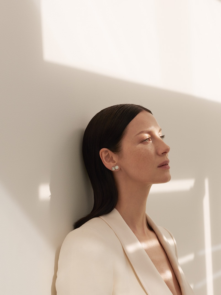 Woman in a cream suit jacket with long dark hair and earrings