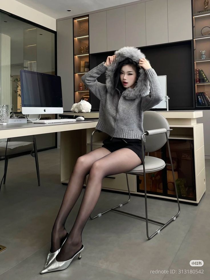 Woman in a fur-hooded sweater, black shorts, and pantyhose sitting indoors