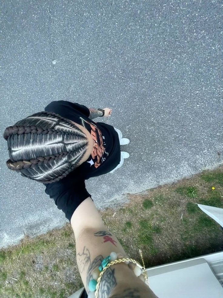 Person with cornrows and tattoos, wearing a t-shirt and bracelet, viewed from above