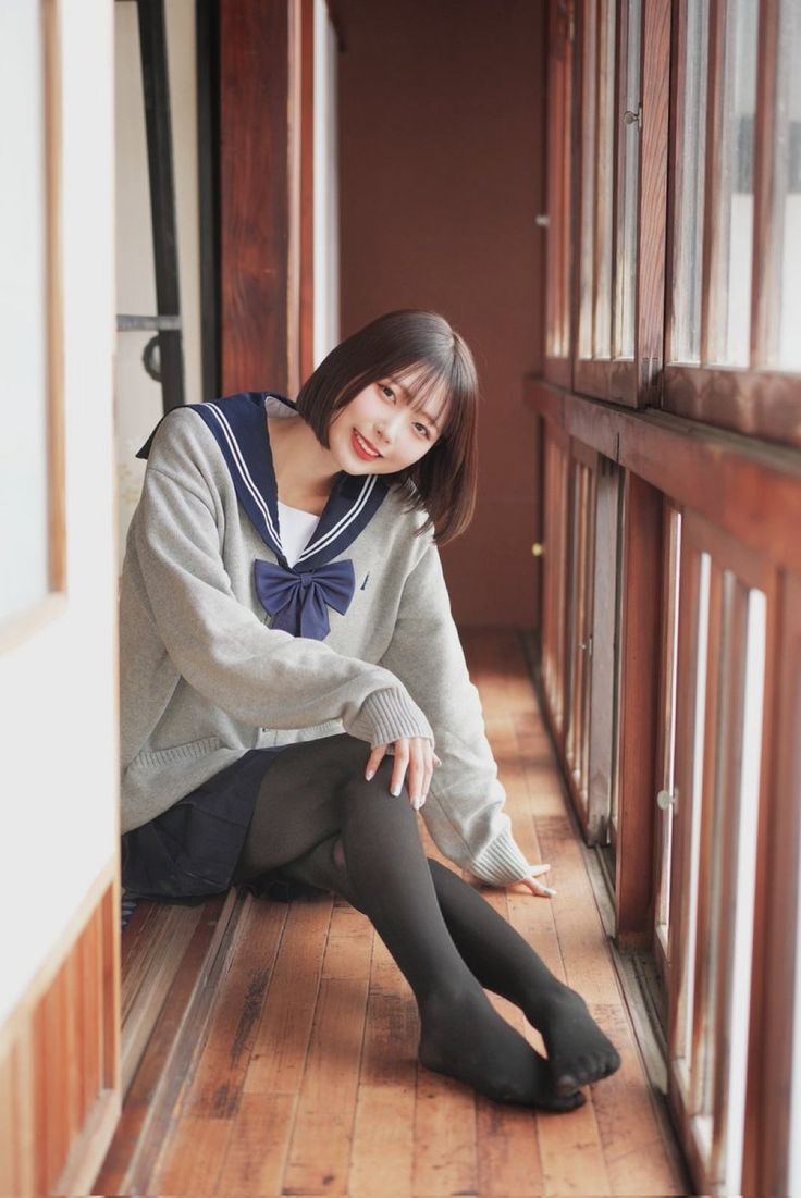 Woman in a school uniform and black tights sitting on a wooden floor indoors