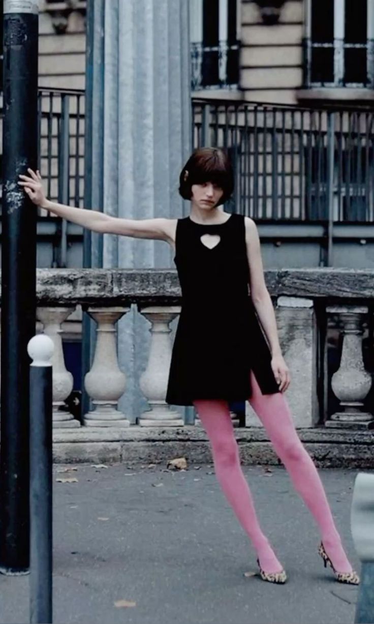 Woman in a black dress and pink tights posing on a street