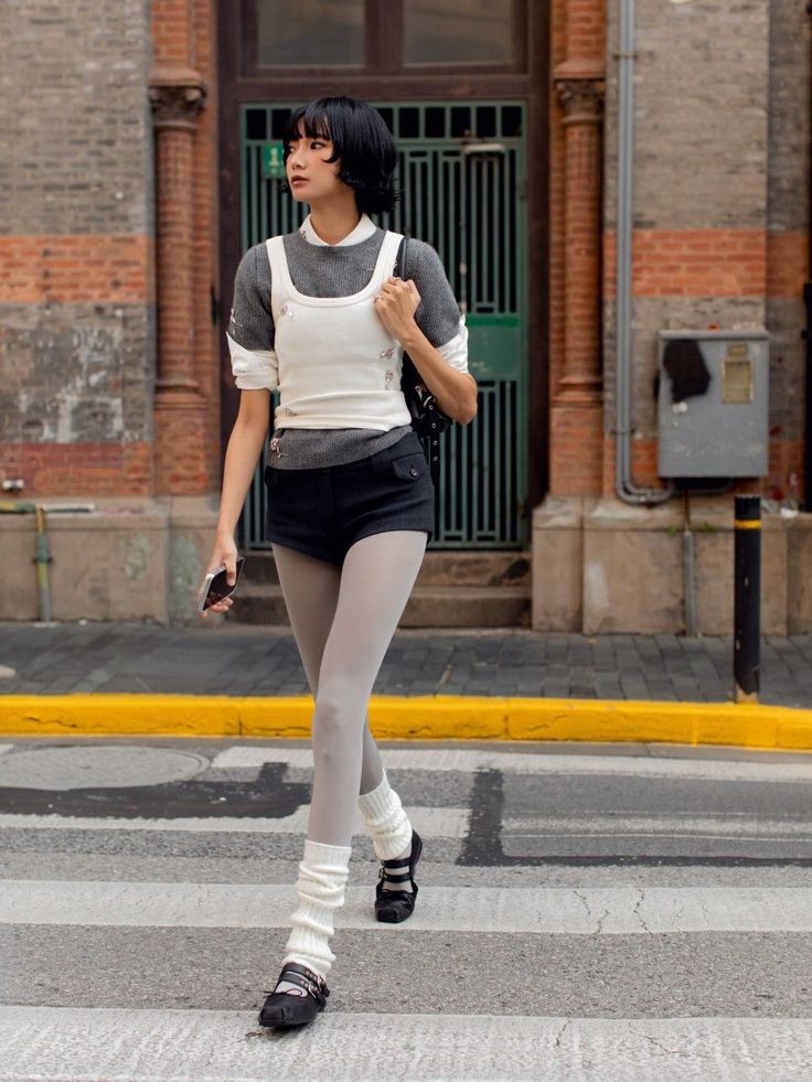Woman with short black hair wearing layered clothing and leg warmers on a crosswalk