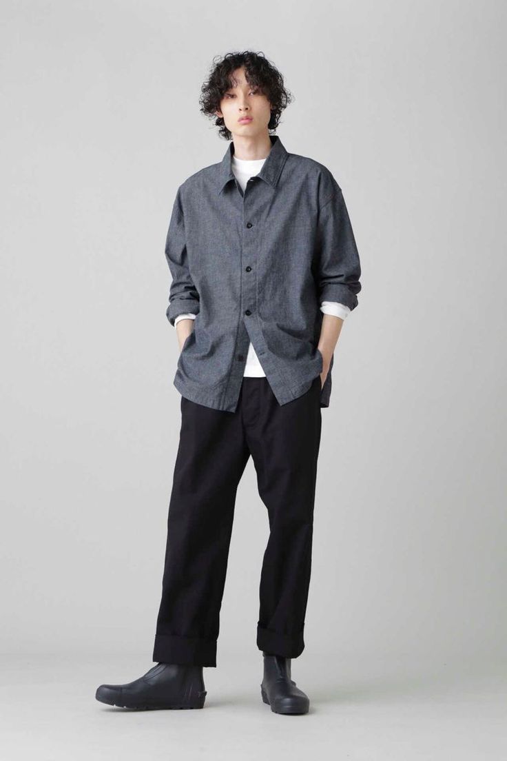 Person with curly hair wearing a denim shirt and black pants in a studio