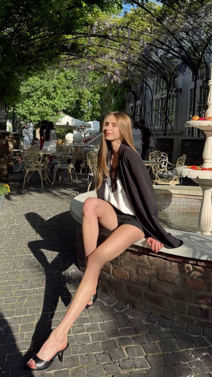 Woman in shorts and a blazer sitting outdoors at a cafe in sunlight