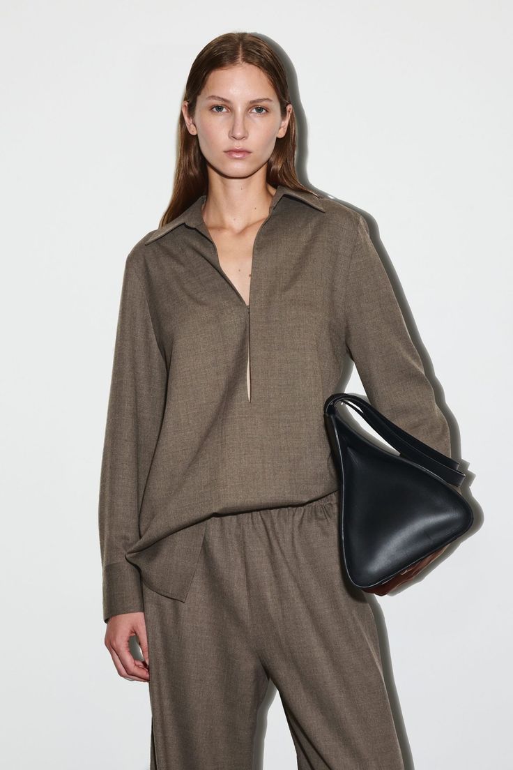 Woman in a brown shirt and pants holding a black bag in a studio