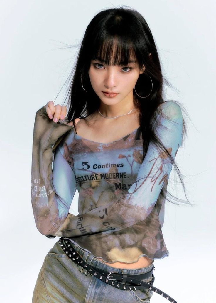Woman with long black hair and bangs wearing a sheer top and jeans
