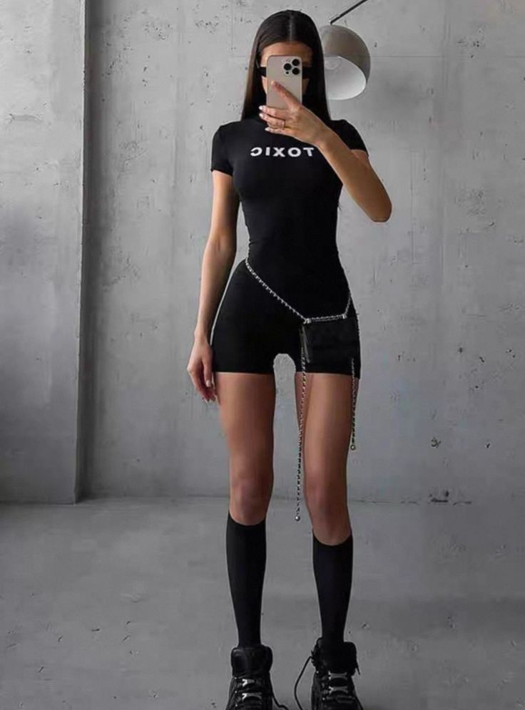 Woman in a black romper with a chain belt taking a mirror selfie
