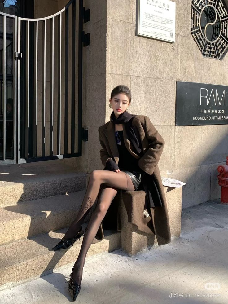 Woman in a brown coat and black tights sitting outdoors