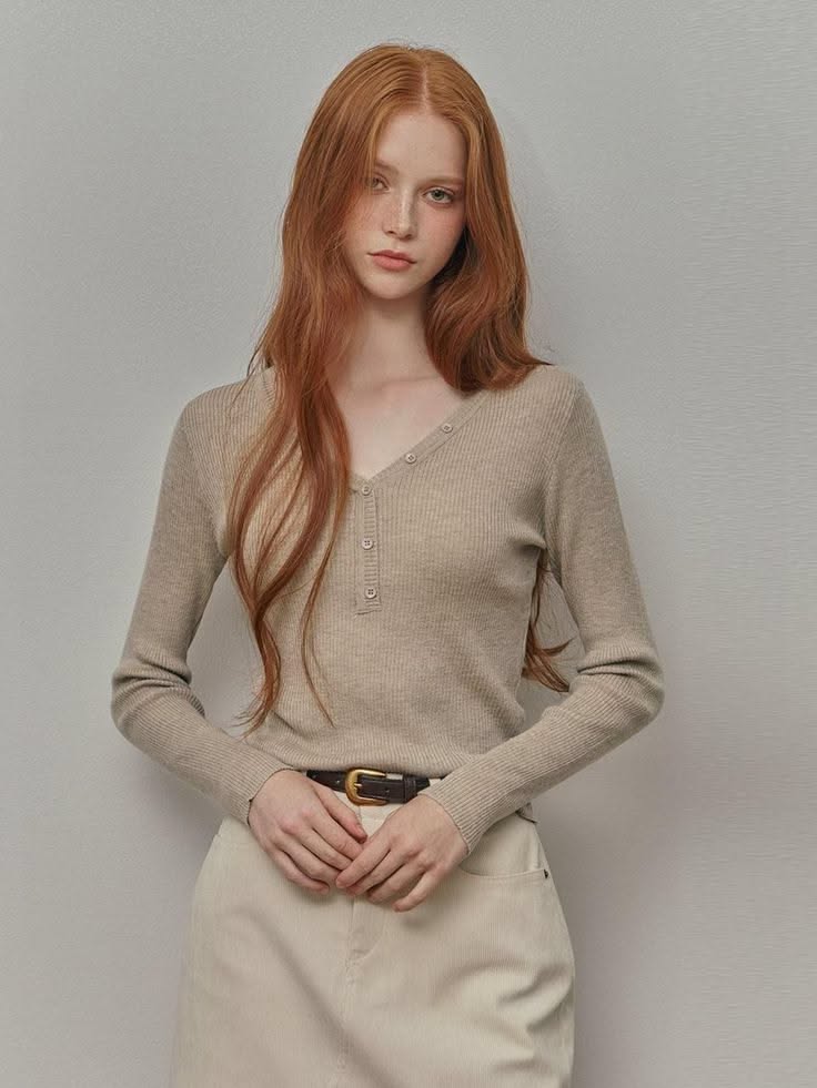 Woman with long red hair and freckles wearing a ribbed v-neck top and light pants