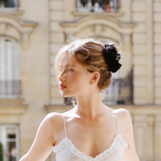 Blonde woman with an updo and white top outdoors in soft lighting