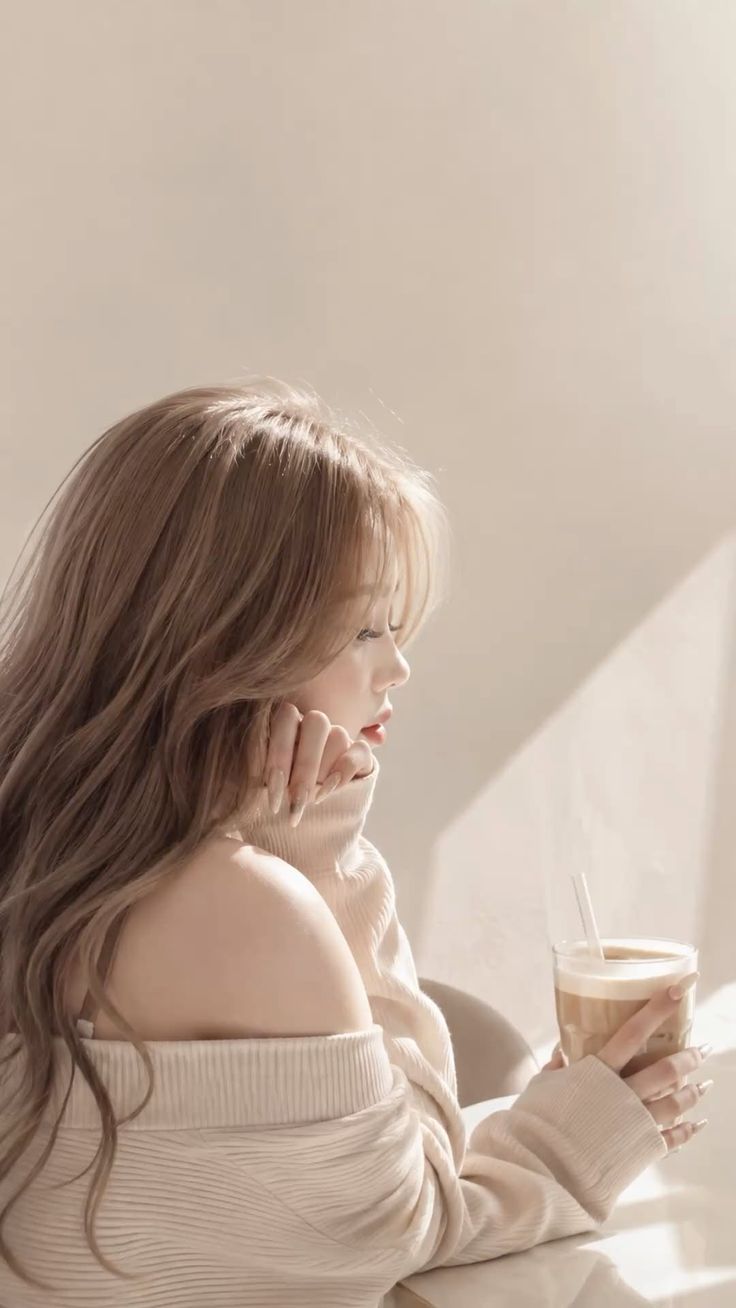 Woman with long hair in an off-shoulder sweater holding an iced coffee