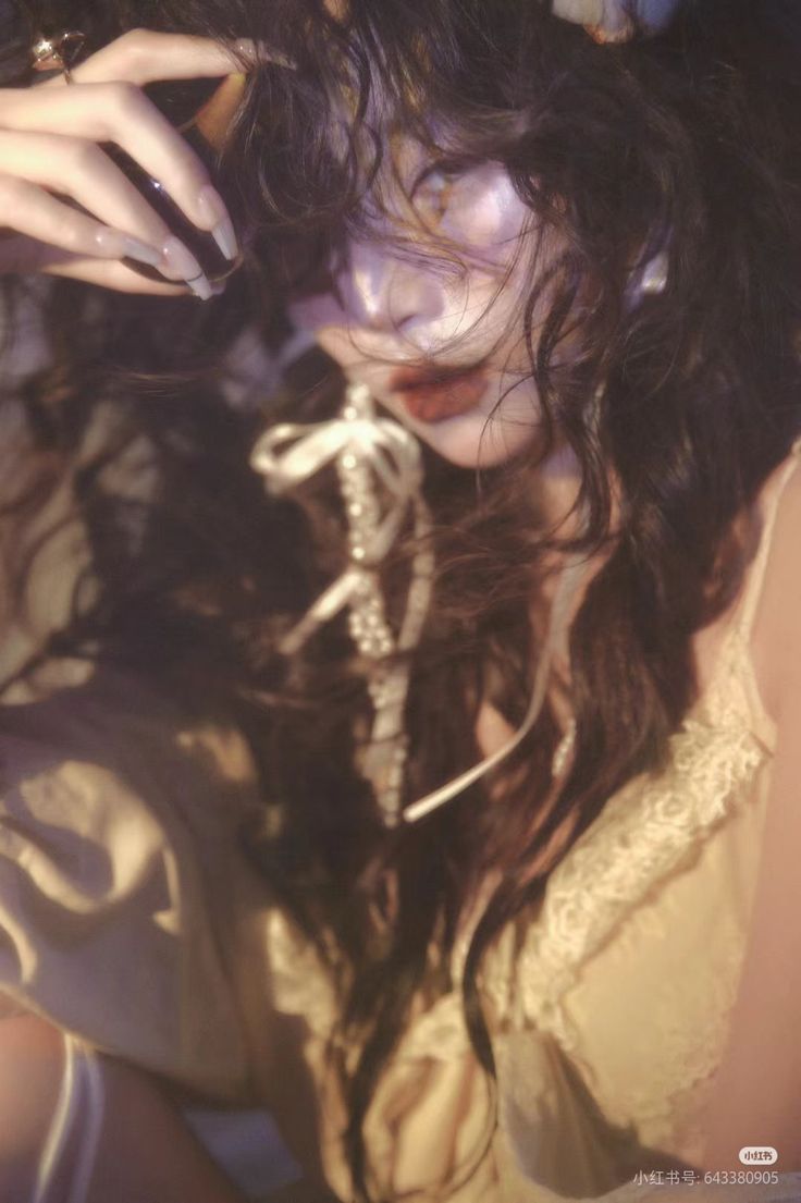 Woman with long dark hair and red lipstick, wearing a top with lace trim