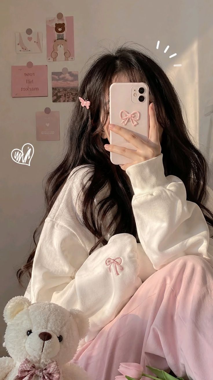 Person with long dark hair taking a mirror selfie with a teddy bear