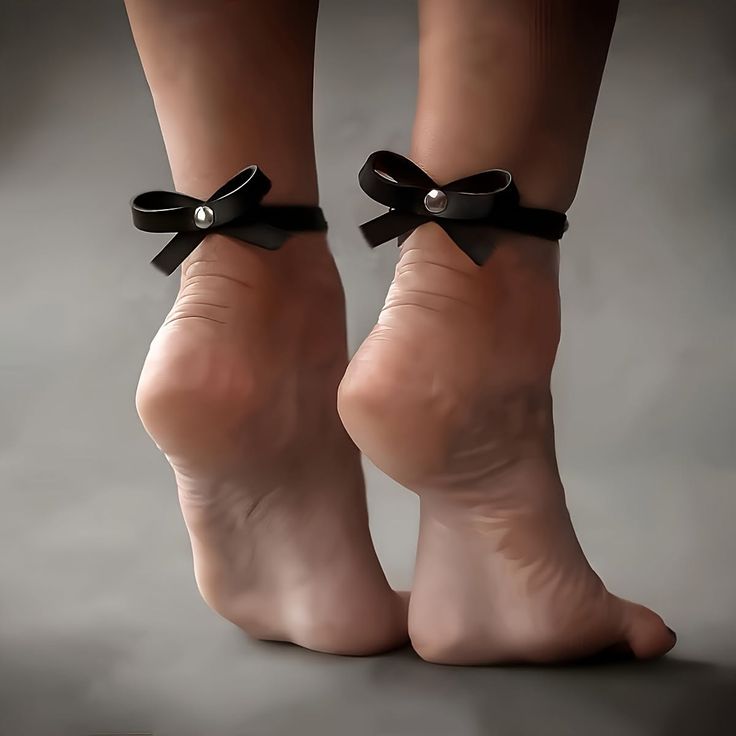 Bare feet with black bow anklets against a grey background
