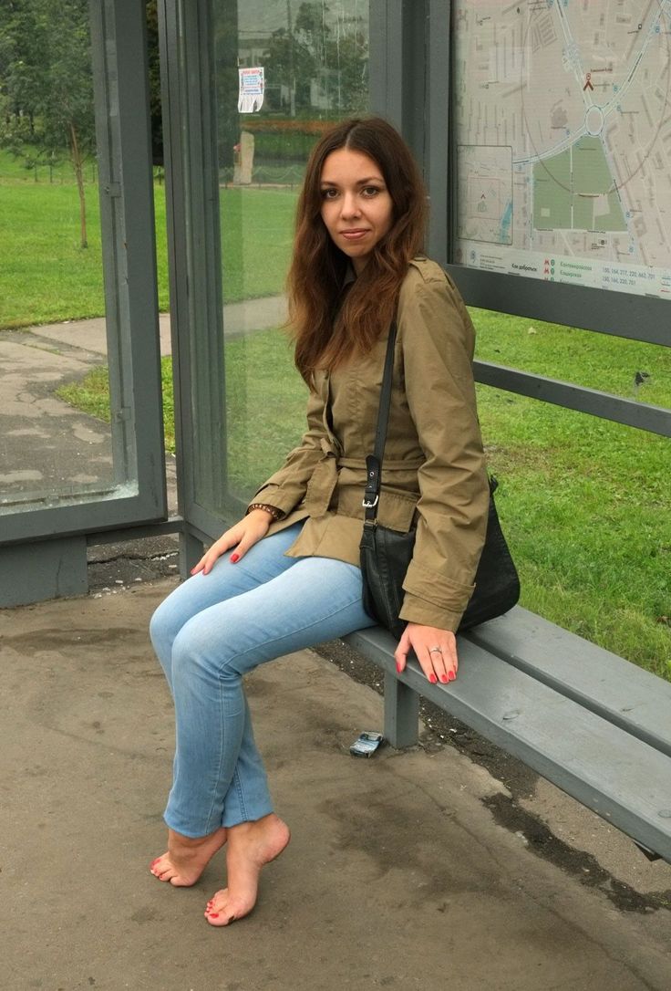 Woman with long hair sitting barefoot at a bus stop