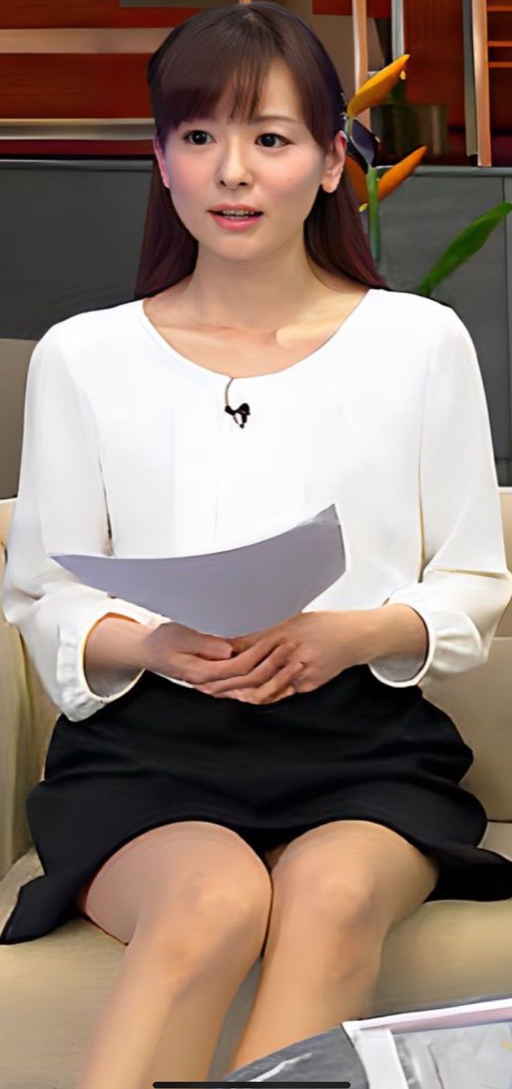 Woman in a white blouse and black skirt with nude pantyhose sitting indoors
