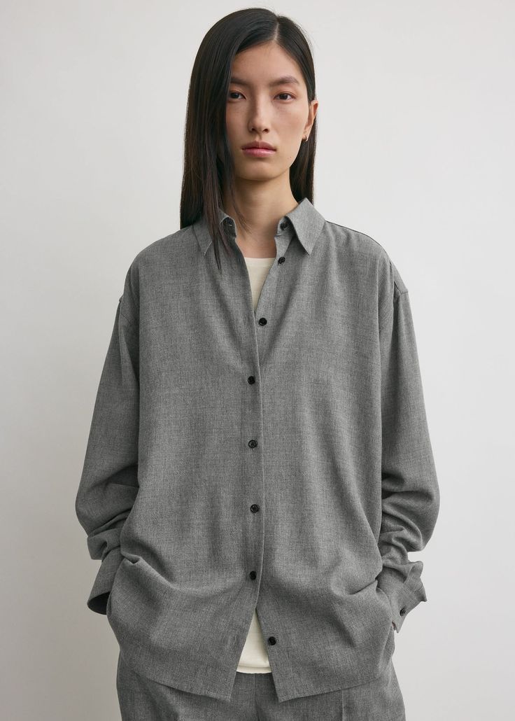 Woman with long dark hair wearing an oversized grey shirt in a studio