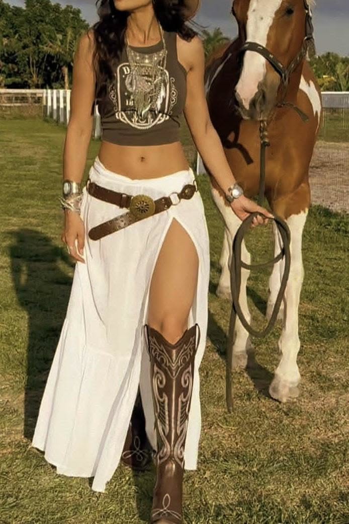 Woman in a crop top and long skirt with a horse in an outdoor setting