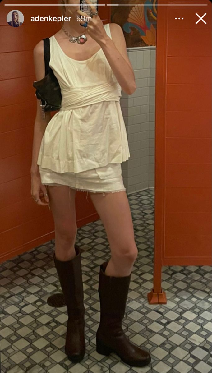 Person in a white top and mini skirt with knee high boots taking a mirror selfie