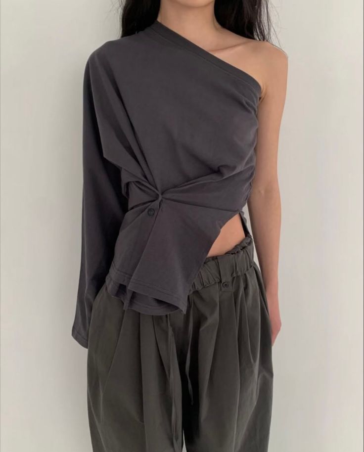 Woman in a dark one-shoulder top with exposed skin and loose pants