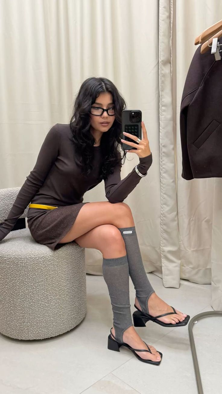 Woman in a brown dress and knee socks taking a mirror selfie indoors