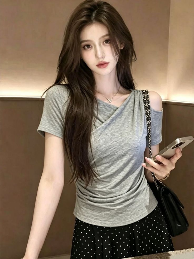 Woman with long hair wearing a gray top and polka dot skirt, holding a phone