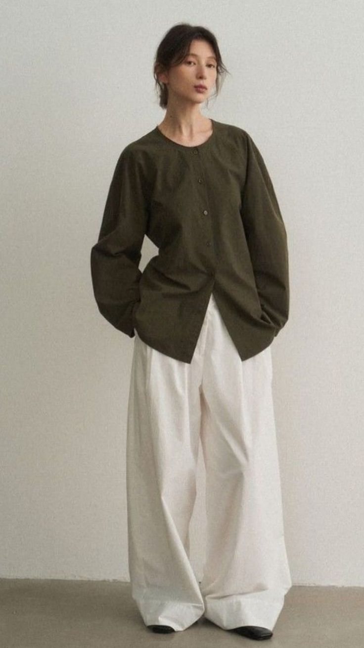 Woman in a dark green shirt and white wide-leg pants against a neutral background